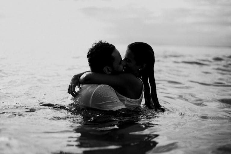 A romantic embrace and kiss in the ocean, captured in black and white.