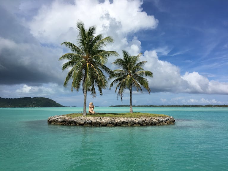 Idyllic tropical scene with a small island, palm trees, and turquoise water under a bright sky.