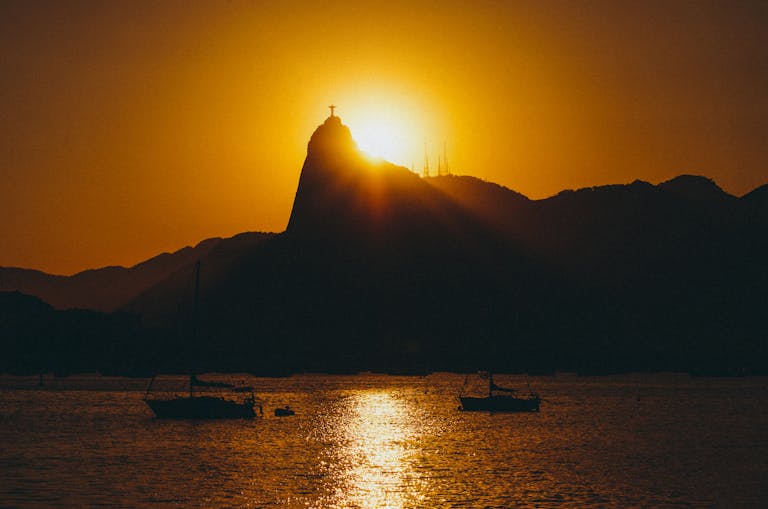 Silhouette of Sugarloaf Mountain at sunset with boats and calm sea in Rio de Janeiro, Brazil.