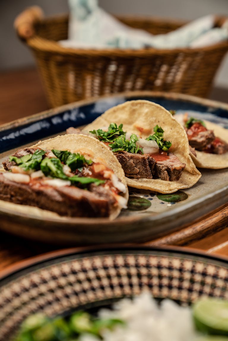 Three mouth-watering Mexican tacos served on a platter with fresh cilantro and onions.