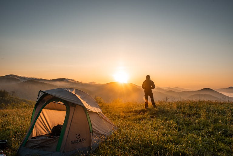 A camper enjoys the sunrise in a mountain setting with a tent. Perfect nature escape.