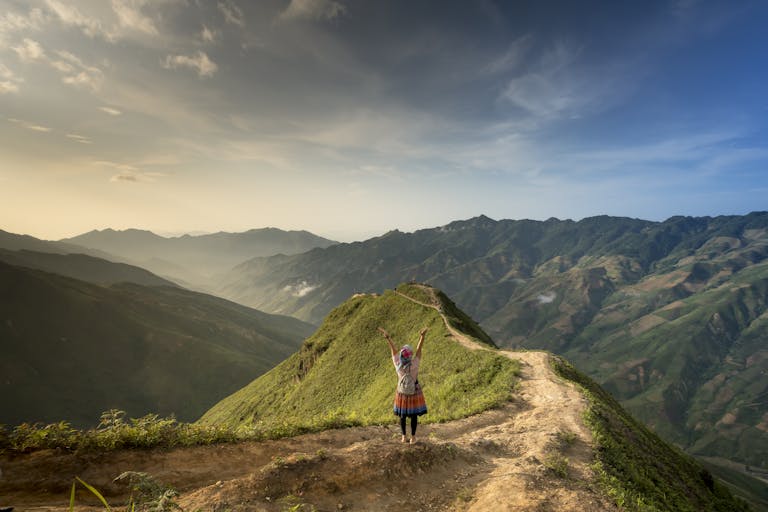 A hiker raises arms in joy on a mountain ridge, bathed in sunrise glow.