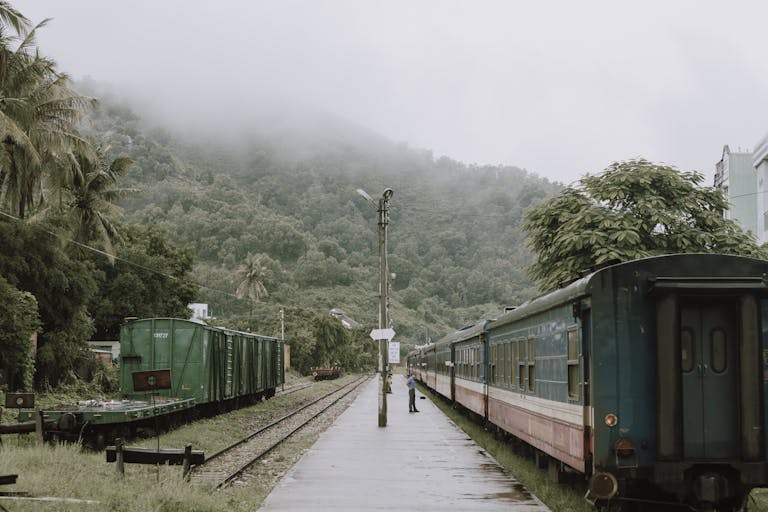 A scenic train station surrounded by misty mountains in Qui Nhon, Vietnam, showcasing vintage locomotives and lush greenery.