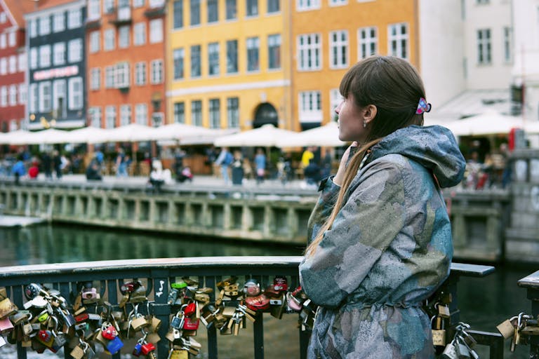 A woman gazes at Nyhavn, Copenhagen, surrounded by love padlocks and colorful buildings.