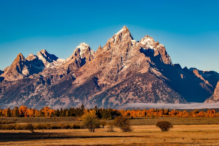 Breathtaking autumn landscape of Grand Teton with snow-capped peaks and colorful trees.