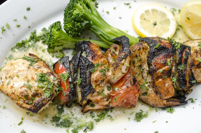 Delicious grilled seafood skewers with vegetables and lemon on a white plate.