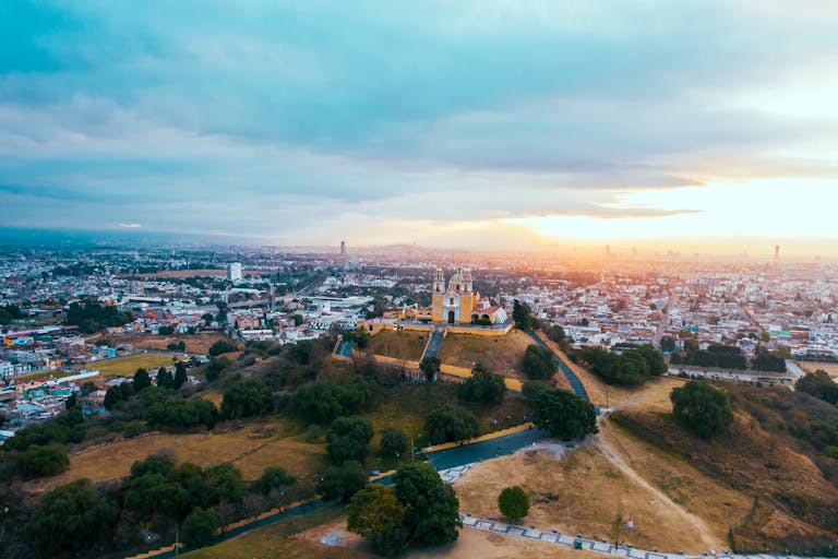 Majestic aerial view of Cholula Pyramid and cityscape at sunset, showcasing rich cultural landscape.