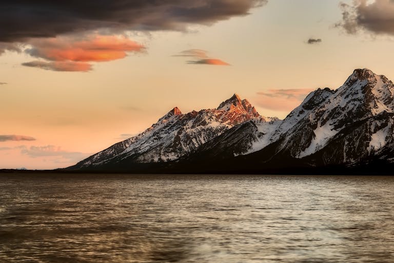 Majestic view of snow-capped mountains with serene water at sunset, creating a stunning natural landscape.