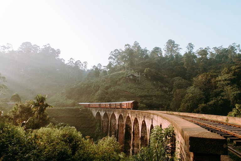 Scenic view of Nine Arches Bridge with train passing through lush greenery in Sri Lanka.