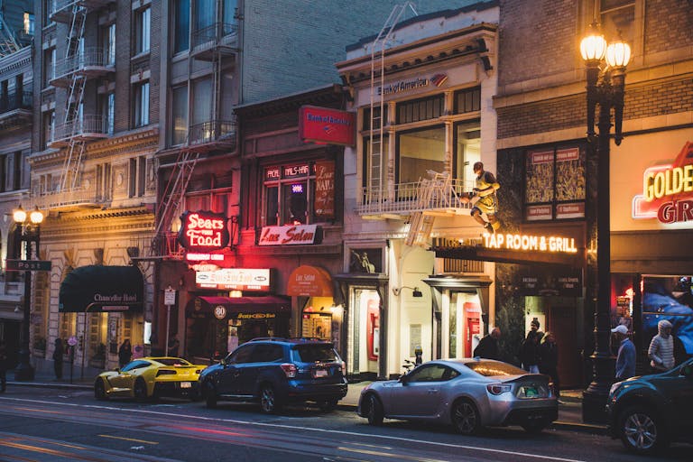 Vibrant city street in San Francisco with neon lights and parked cars at evening.