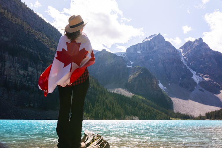 A woman stands wrapped in a Canadian flag, admiring the scenic Moraine Lake and mountains.