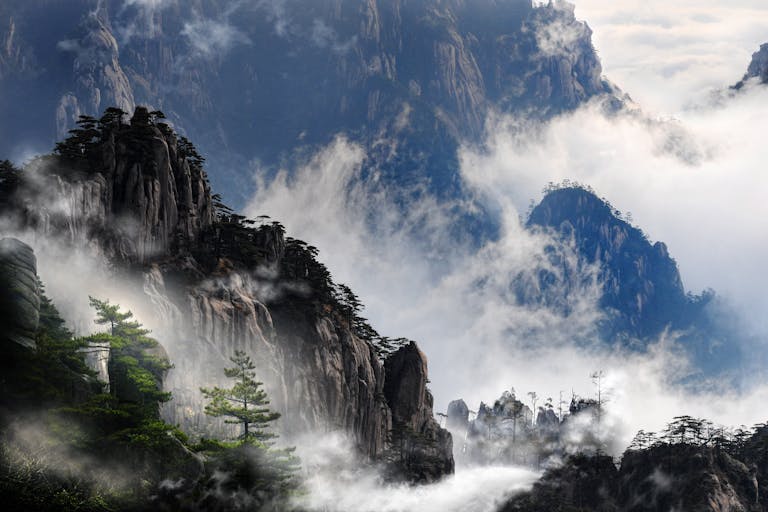 Misty mountain peaks of Huangshan, China enveloped in fog, creating a serene and dramatic landscape.