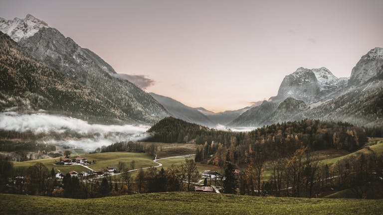 Serene winter landscape of an alpine village at sunrise, surrounded by misty mountains and lush forests.