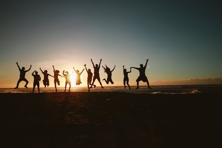 Silhouette of a group of friends jumping on a beach at sunset, expressing joy and freedom.