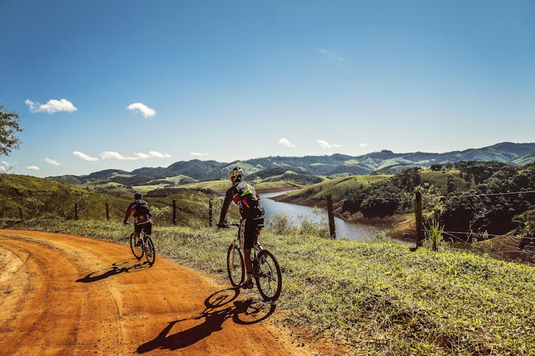 Two cyclists riding on a dirt trail with stunning mountain views and clear skies.